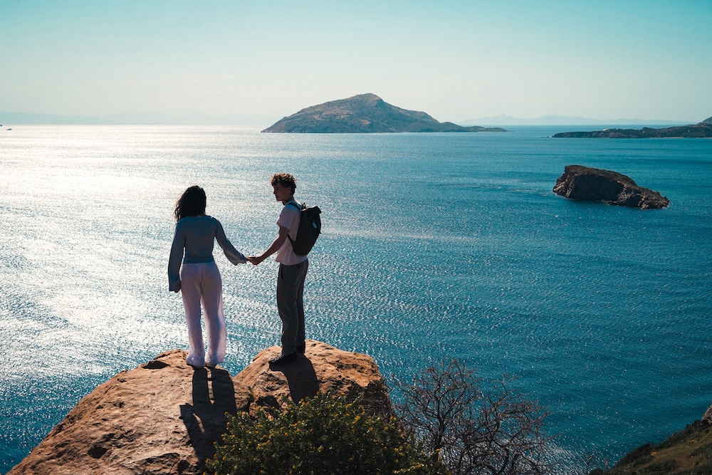 THINK Global School student Liam standing on a rocky cliff overlooking the Aegean Sea near Cape Sounion, Greece, during a 2026 educational term.